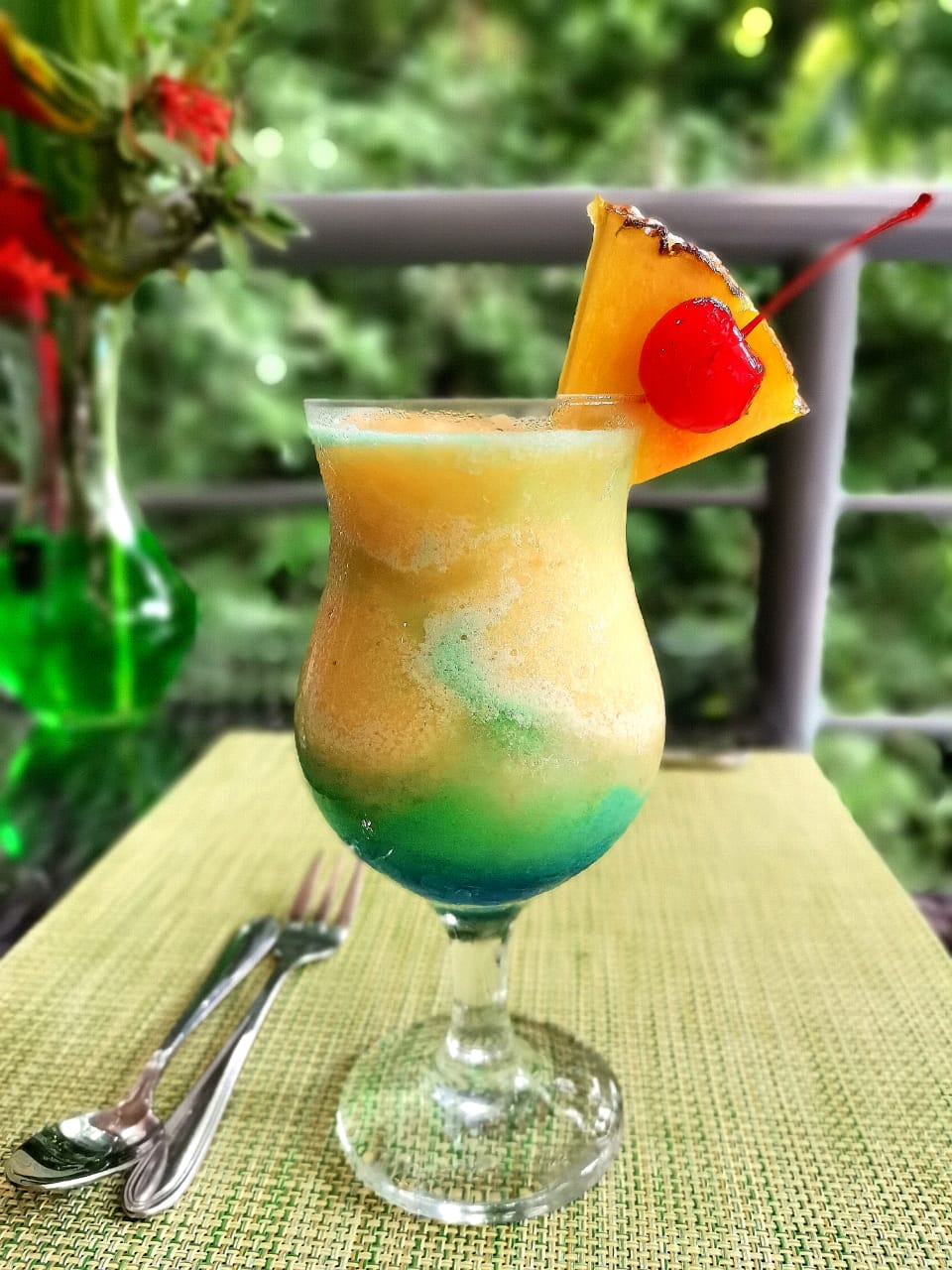 Layered tropical cocktail garnished with pineapple and cherry at Dante's beach setup