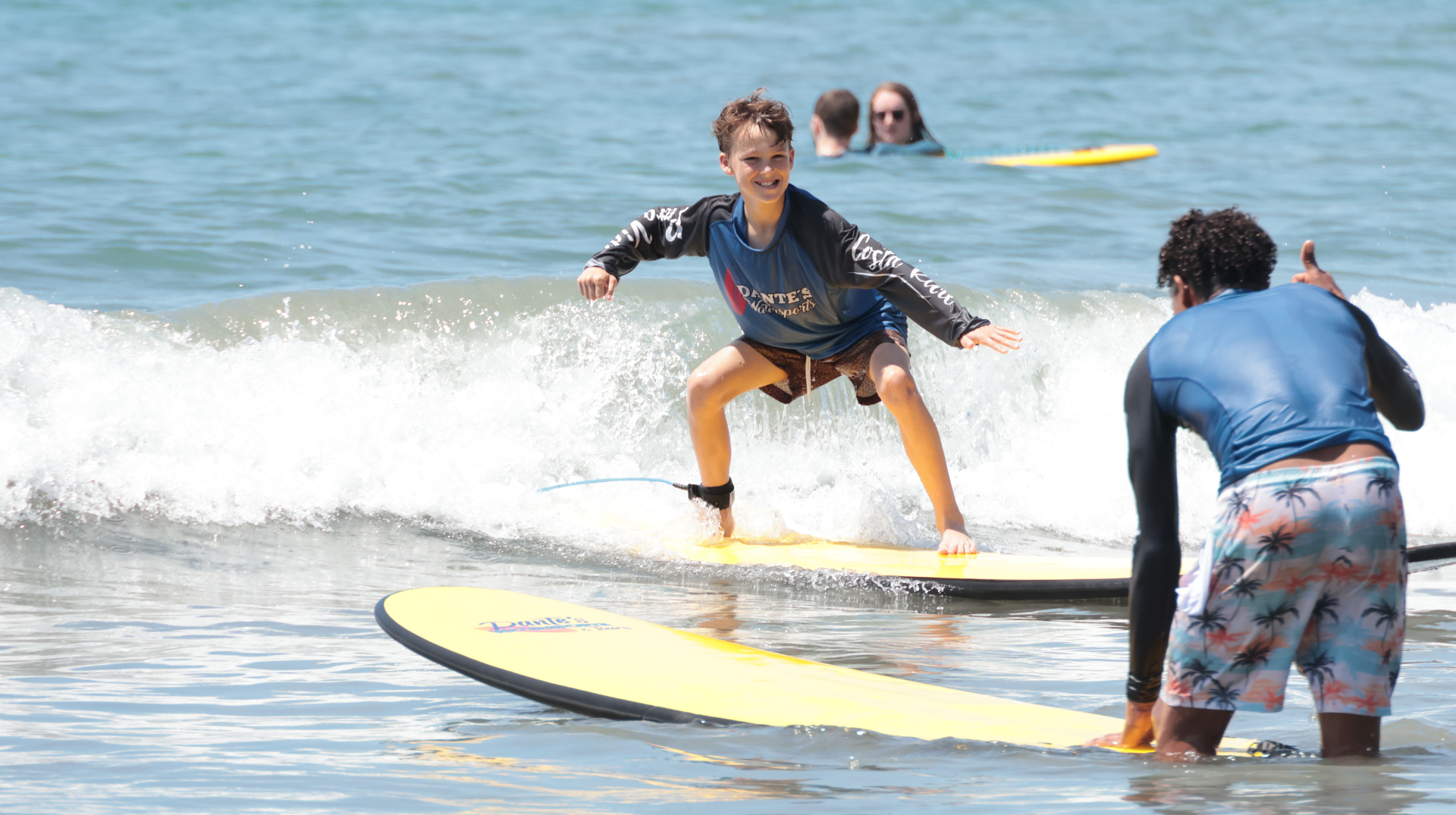 Student riding a wave on a Dante's Watersports yellow soft-top board, Playa Espadilla